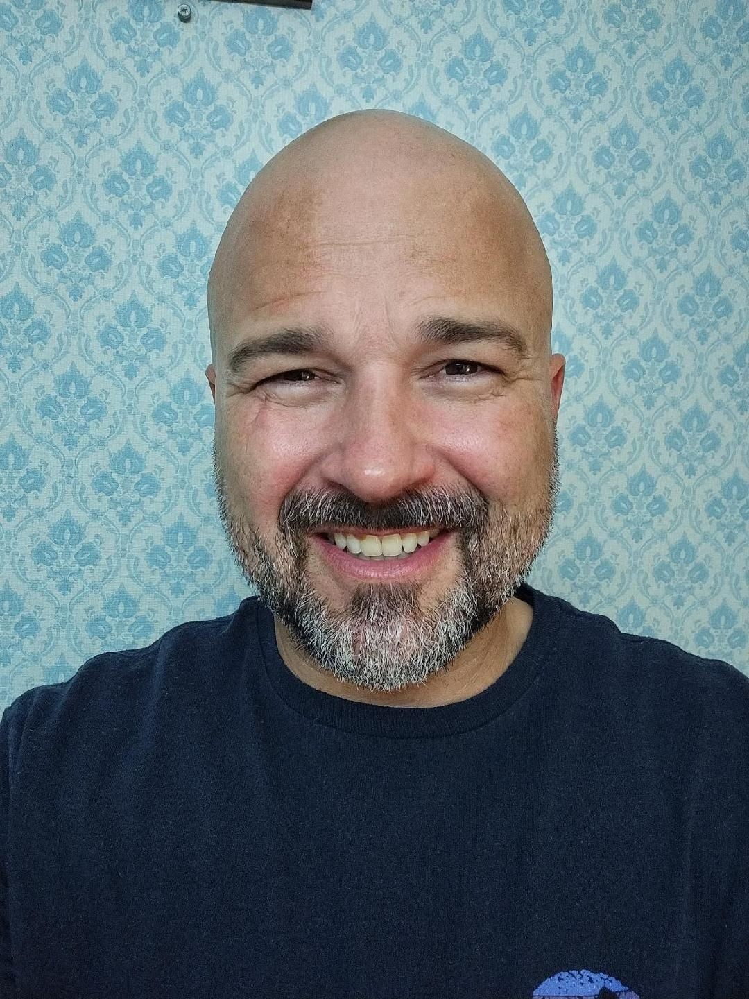 Person wearing a dark shirt, standing in front of a blue patterned wallpaper.